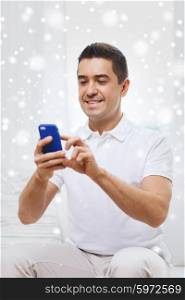 technology, people, lifestyle and communication concept - happy man with smartphone at home over snow effect