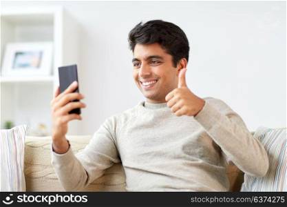 technology, people, lifestyle and communication concept - happy man with smartphone having video call at home and showing thumbs up. happy man having video call on smartphone at home