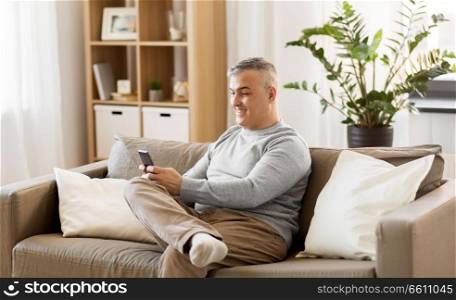 technology, people, lifestyle and communication concept - man with smartphone sitting on sofa at home. man with smartphone sitting on sofa at home
