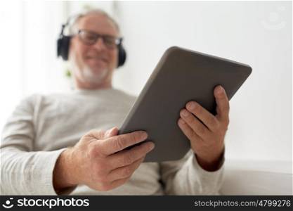 technology, people, lifestyle and distance learning concept - close up of happy senior man with tablet pc computer and headphones listening to music at home