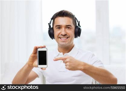 technology, people, lifestyle and distance learning concept - happy man in headphones showing smartphone black blank screen and listening to music at home