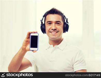 technology, people, lifestyle and distance learning concept - happy man in headphones showing smartphone black blank screen and listening to music at home