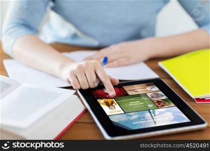technology, people, media and internet concept - close up of student woman with news on tablet pc computer screen and notebook at home