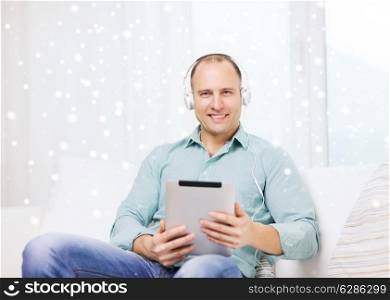 technology, people, winter and leisure concept - smiling man in headphones with tablet pc sitting on couch at home
