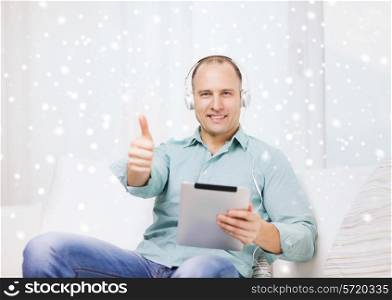 technology, people, winter, gesture and leisure concept - smiling man in headphones with tablet pc sitting on couch and showing thumbs up at home