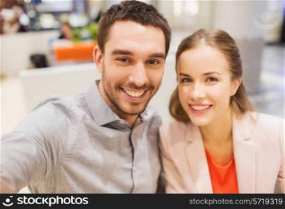 technology, photographing, and people concept - happy couple taking selfie with smartphone or camera in mall or office
