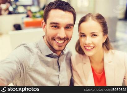 technology, photographing, and people concept - happy couple taking selfie with smartphone or camera in mall or office