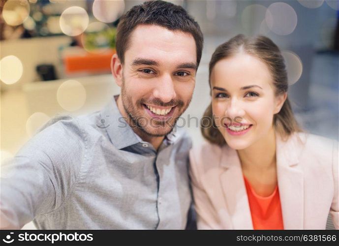 technology, photographing, and people concept - happy couple taking selfie with smartphone or camera in mall or office. happy couple taking selfie in mall or office