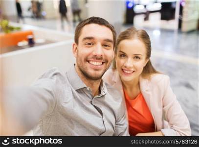 technology, photographing, and people concept - happy couple taking selfie with smartphone or camera in mall