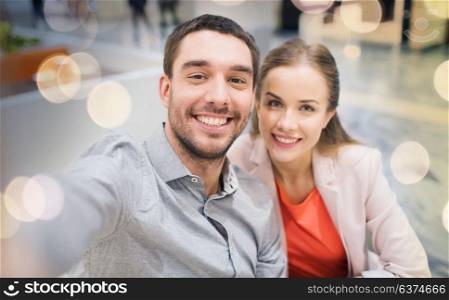 technology, photographing, and people concept - happy couple taking selfie with smartphone or camera in mall. happy couple taking selfie in mall or office