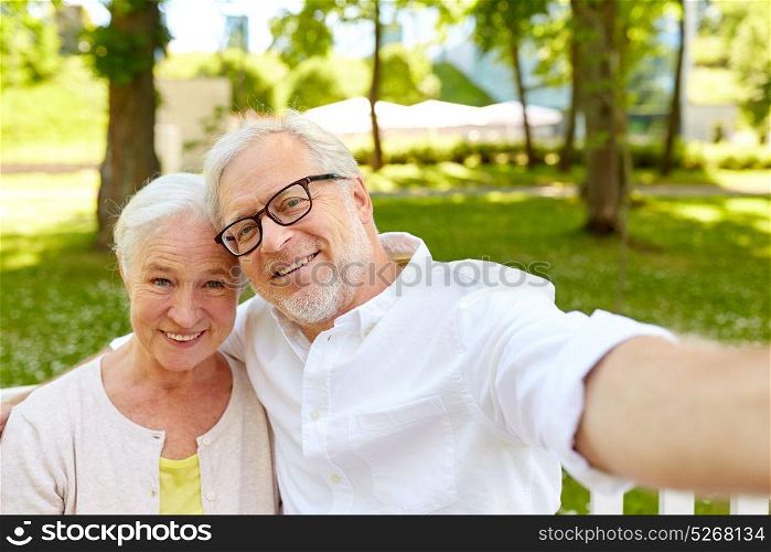 technology, relationship and old people concept - happy senior couple taking selfie and hugging at summer park . senior couple taking selfie at summer park