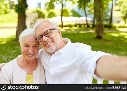 technology, relationship and old people concept - happy senior couple taking selfie and hugging at summer park . senior couple taking selfie at summer park