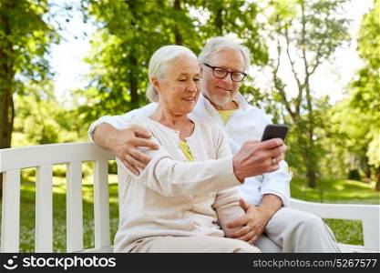technology, relationship and old people concept - happy senior couple with smartphone taking selfie and hugging in summer. senior couple with smartphone taking selfie