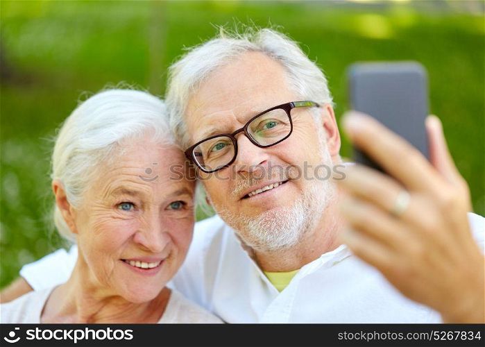 technology, relationship and old people concept - happy senior couple with smartphone taking selfie and hugging in summer. senior couple with smartphone taking selfie in summer