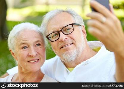 technology, relationship and old people concept - happy senior couple with smartphone taking selfie and hugging in summer. senior couple with smartphone taking selfie in summer