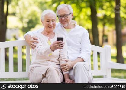 technology, relationship and old people concept - happy senior couple with smartphone taking selfie and hugging at park. senior couple taking selfie by smartphone at park
