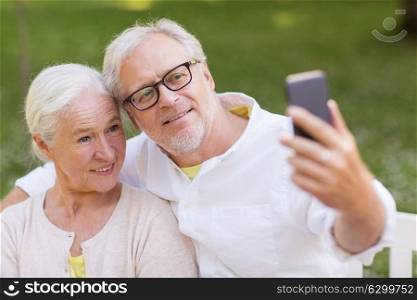 technology, relationship and old people concept - happy senior couple with smartphone taking selfie and hugging at summer park. senior couple taking selfie by smartphone at park