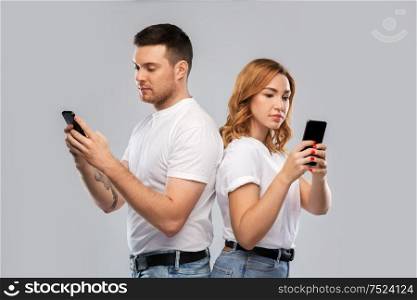 technology, relationships and people concept - couple in white t-shirts with smartphones over grey background. couple in white t-shirts with smartphones