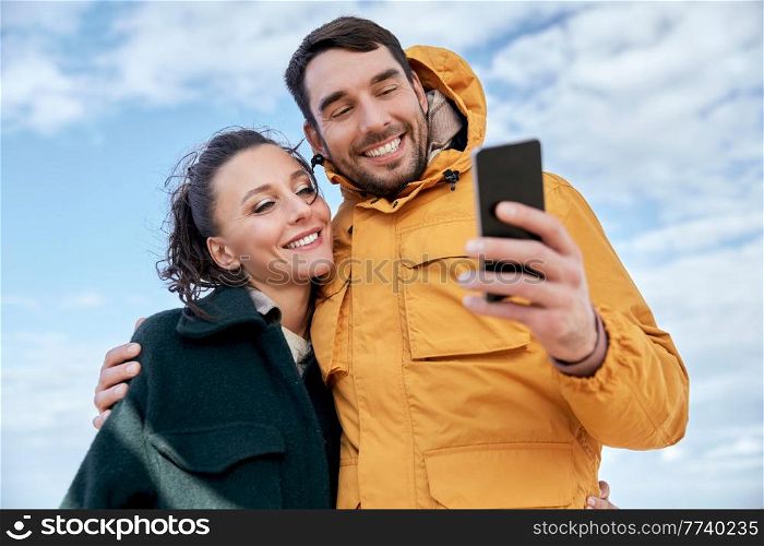 technology, relationships and people concept - happy couple with smartphone on autumn beach. couple with smartphone on autumn beach