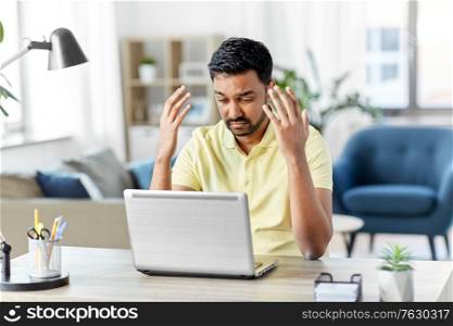 technology, remote job and business concept - disappointed indian man with laptop computer working at home office. indian man with laptop working at home office