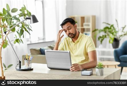 technology, remote job and business concept - disappointed indian man with laptop computer working at home office. indian man with laptop working at home office