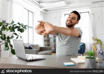 technology, remote job and business concept - happy smiling man with laptop computer stretching at home office. happy man with laptop stretching at home office