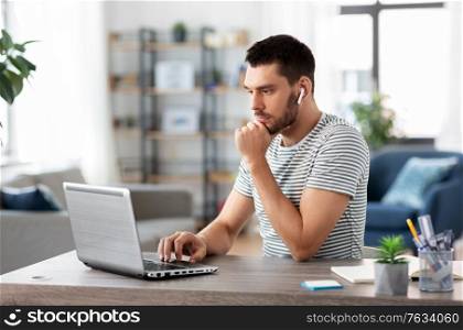 technology, remote job and business concept - man with laptop computer and earphones working at home office. man with laptop and earphones at home office