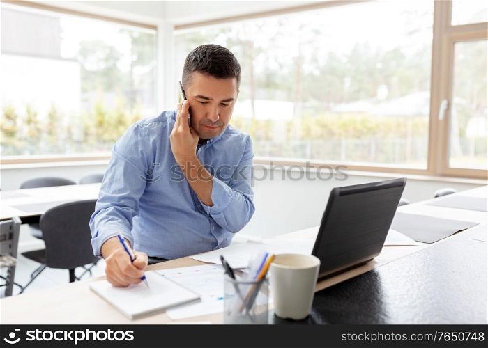 technology, remote job and business concept - middle-aged man calling on smartphone and writing to notebook at home office. man calling on smartphone at home office