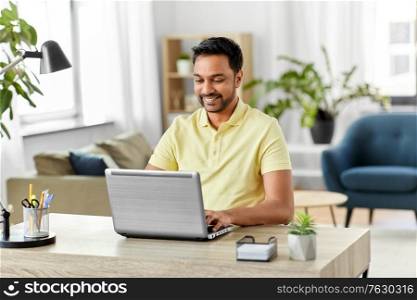 technology, remote job and lifestyle concept - happy smiling indian man with laptop computer working at home office. indian man with laptop working at home office