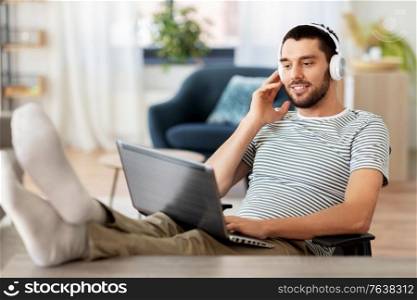 technology, remote job and lifestyle concept - happy smiling man with laptop computer and headphones resting feet on table at home office. happy man with laptop and headphones at home