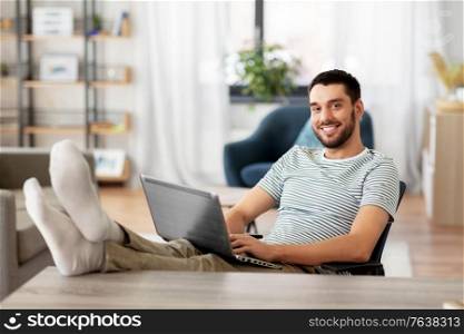 technology, remote job and lifestyle concept - happy smiling man with laptop computer resting feet on table at home office. man with laptop resting feet on table at home