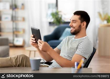 technology, remote job and lifestyle concept - happy smiling man with tablet pc computer resting feet on table at home office. man with tablet pc resting feet on table at home