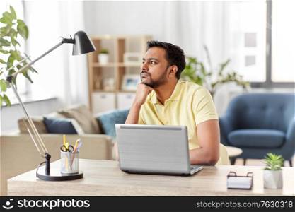 technology, remote job and lifestyle concept - indian man with laptop computer thinking at home office. indian man with laptop thinking at home office