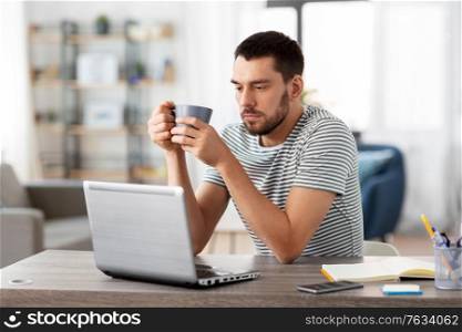 technology, remote job and lifestyle concept - man with laptop computer drinking coffee or tea at home office. man with laptop drinking coffee at home office