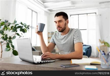 technology, remote job and lifestyle concept - man with laptop computer drinking coffee or tea at home office. man with laptop drinking coffee at home office