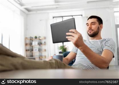 technology, remote job and lifestyle concept - man with tablet pc computer resting feet on table at home office. man with tablet pc resting feet on table at home