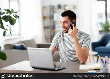 technology, remote job and people concept - happy smiling man with laptop computer calling on smartphone at home office. man with laptop calling on phone at home office