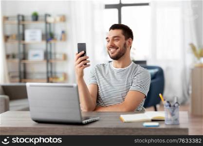 technology, remote job and people concept - happy smiling man with smartphone and laptop computer working at home office. man with smartphone and laptop at home office