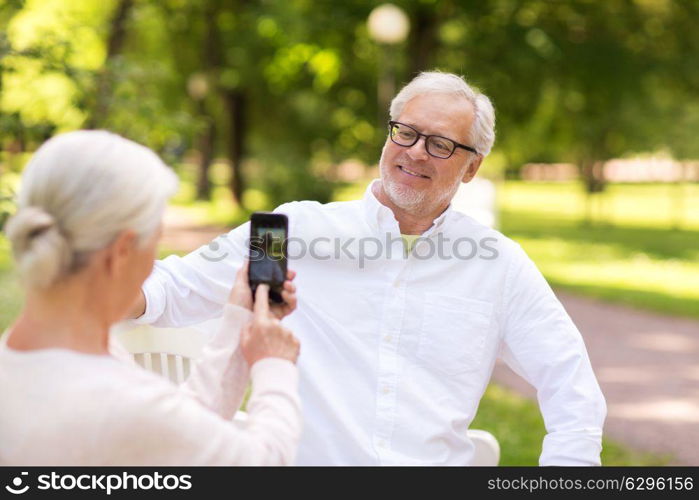 technology, retirement and old people concept - happy smiling senior couple with smartphone photographing in summer park. old woman photographing man by smartphone in park