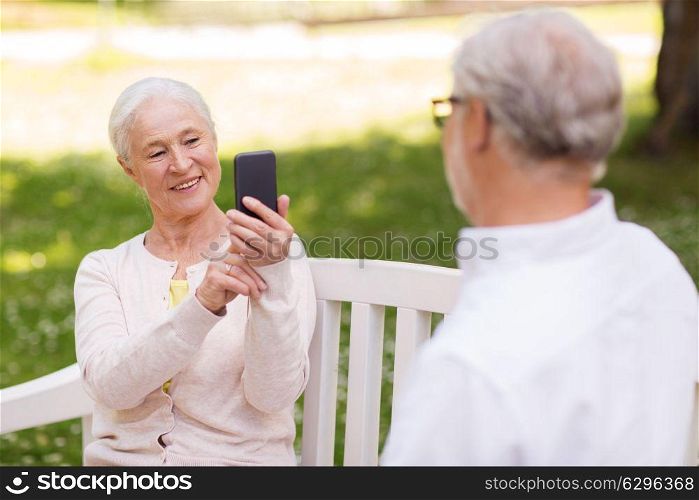 technology, retirement and old people concept - happy smiling senior couple with smartphone photographing in summer park. old woman photographing man by smartphone in park