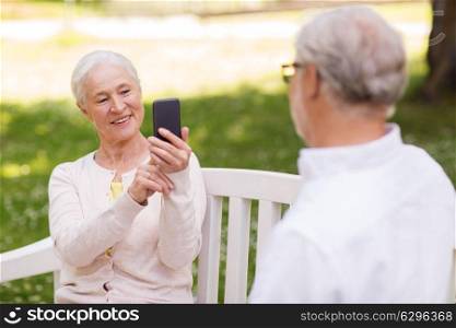 technology, retirement and old people concept - happy smiling senior couple with smartphone photographing in summer park. old woman photographing man by smartphone in park