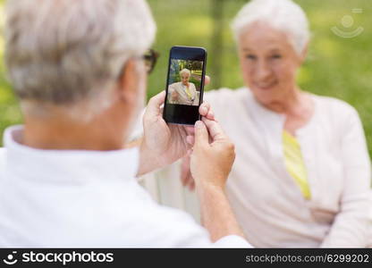 technology, retirement and old people concept - happy smiling senior couple with smartphone photographing in summer park. old woman photographing man by smartphone in park