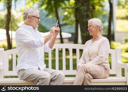 technology, retirement and old people concept - happy smiling senior couple with smartphone photographing in summer park. old woman photographing man by smartphone in park