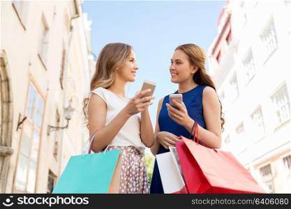technology, sale, cloud computing and people concept - happy young women with shopping bags and smartphones on city street. happy women with shopping bags and smartphones