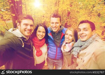 technology, season, friendship and people concept - group of smiling men and women taking selfie with smartphone or camera in autumn park