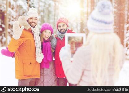 technology, season, friendship and people concept - group of smiling men and women taking picture with tablet pc computer in winter forest