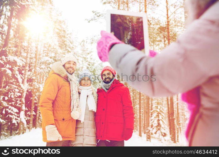 technology, season, friendship and people concept - group of smiling men and women taking picture with tablet pc computer in winter forest