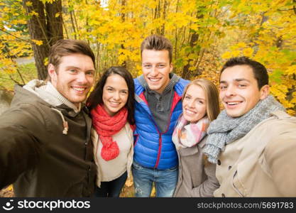 technology, season, friendship and people concept - group of smiling men and women taking selfie with smartphone or camera in autumn park