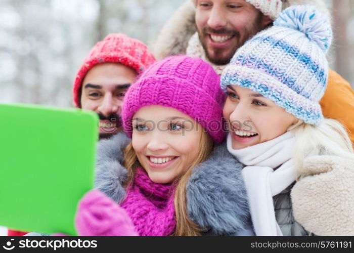 technology, season, friendship and people concept - group of smiling men and women taking selfie tablet pc computer in winter forest