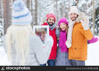 technology, season, friendship and people concept - group of smiling men and women taking picture with tablet pc computer in winter forest